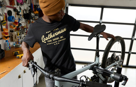 Translation missing: es.Person assembling a bicycle in a workshop wearing a black Leatherman Vintage Tee