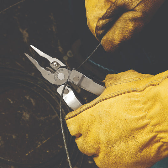 Translation missing: nl. A person wearing yellow leather gloves using a Leatherman Rebar to cut wire