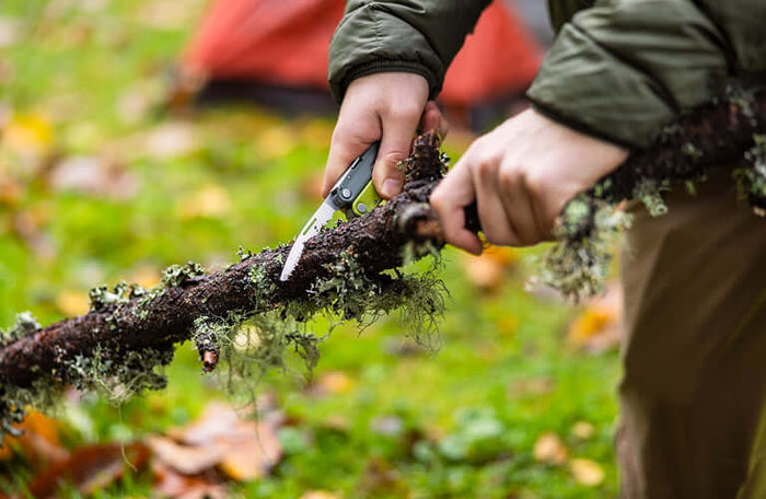 Translation missing: pl.Person using a Mossy Slate Leatherman Rebar saw on a moss-covered branch outdoors