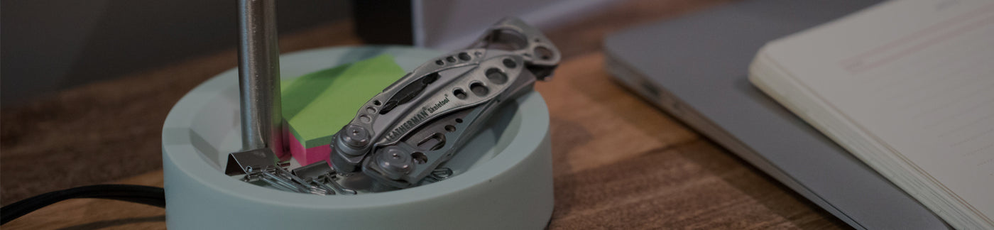 Translation missing: de.Stainless Steel Leatherman Skeletool® resting on a desk organizer beside a notebook and sticky notes in a modern workspace.
