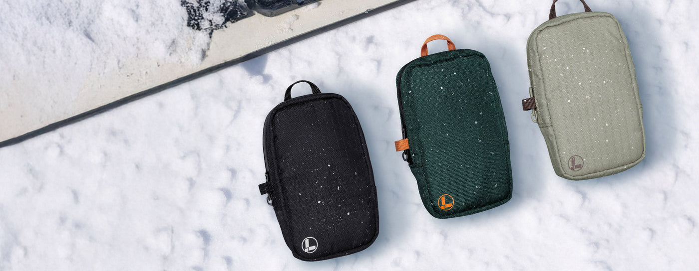 Translation missing: de.Black, hunter green, and mossy fog Leatherman tool pouches on a snowy background with a snowboard