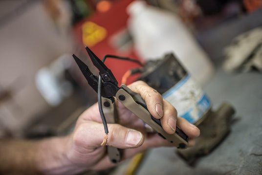 Person holding a Leatherman Coyote Rebar® multi-tool with pliers in a workshop setting.