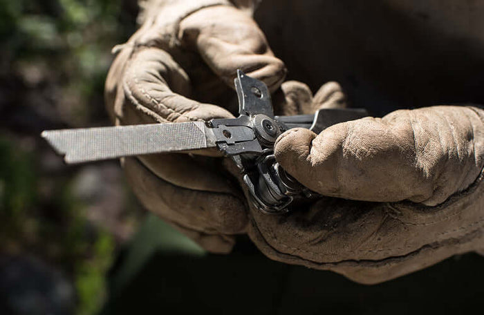 Translation missing: pl.Close-up of hands in gloves holding a Leatherman Surge® multitool with a file attachment