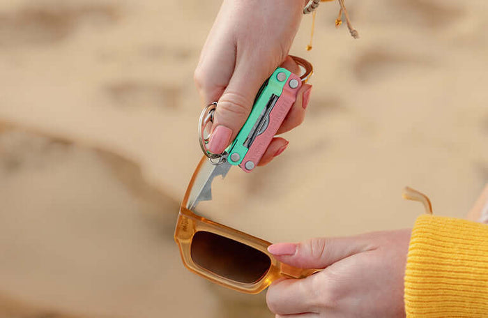 Translation missing: pl.Person using the extra small screwdriver on a Leatherman Micra® in Bayside color to tighten sunglasses on the beach