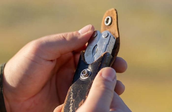 Translation missing: es.Person holding a Leatherman PST 2 multitool in a worn leather case outdoors