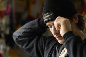 Translation missing: de.A person adjusting a black Leatherman Vintage Beanie while indoors, with the gold embroidered Leatherman logo visible on the front patch