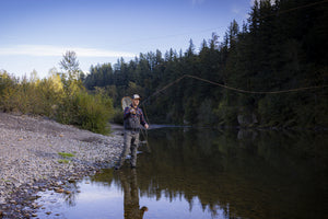 Translation missing: es.A person wearing a beige Leatherman PNW Trucker hat fly-fishing in a river surrounded by trees