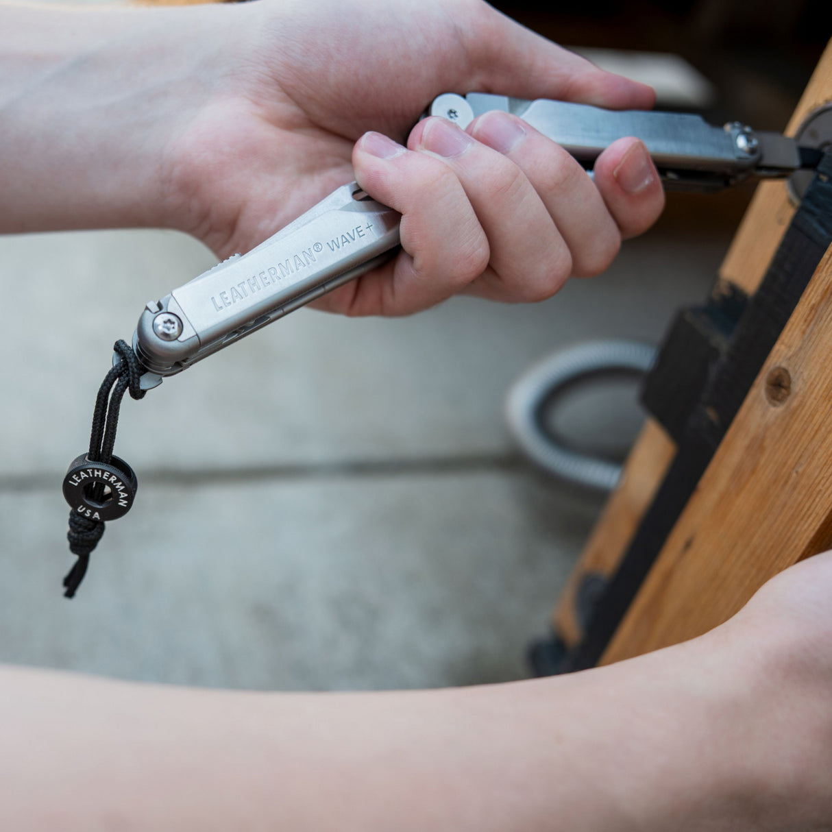Translation missing: pl.Lanyard and bead attached to the deployable leatherman Wave lanyard ring as the tools bit driver is being used on a door