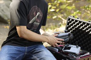 Translation missing: es.A person pulling a drone out of a carrying case while wearing a black Leatherman Blade &amp; Grain Tee with a fixed blade design on the front
