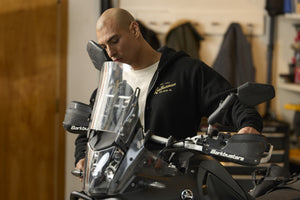 Translation missing: en.A person wearing a black Leatherman Vintage Zip-Up hoodie standing next to a motorcycle in a garage, with the hoodie’s gold Leatherman logo visible on the chest