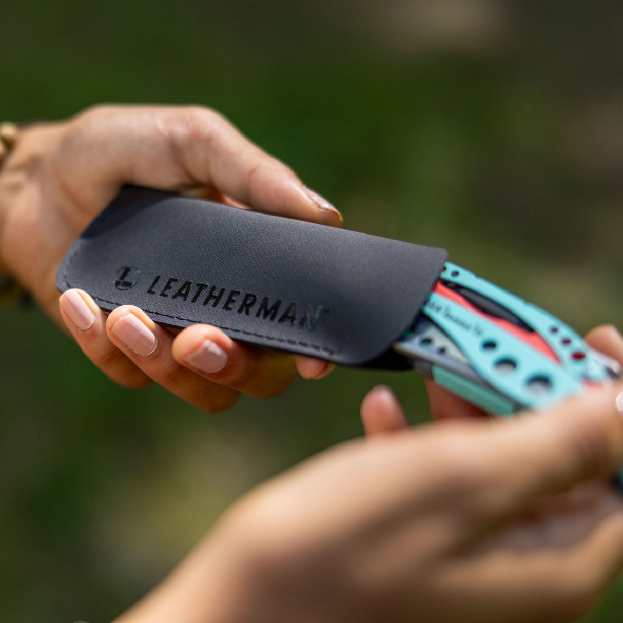 Translation missing: es.A black Leatherman Hypalon tool sleeve held in hand with a partially inserted Paradise-colored Skeletool® CX multi-tool, highlighting the tool’s vibrant design and protective carrying case