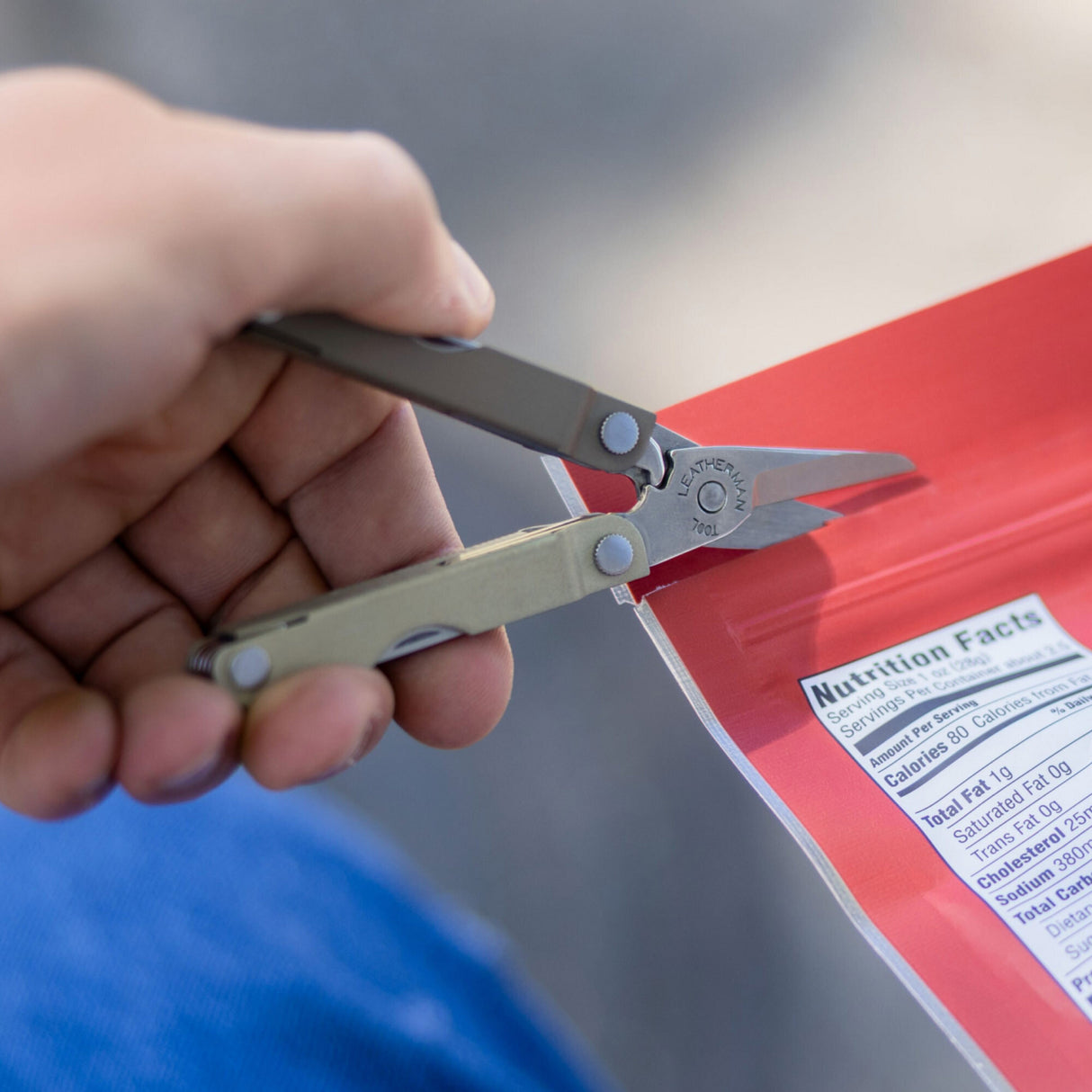 Translation missing: es.A Winter Fog colored Leatherman Micra being used to cut open red snack packaging with its spring-action scissors