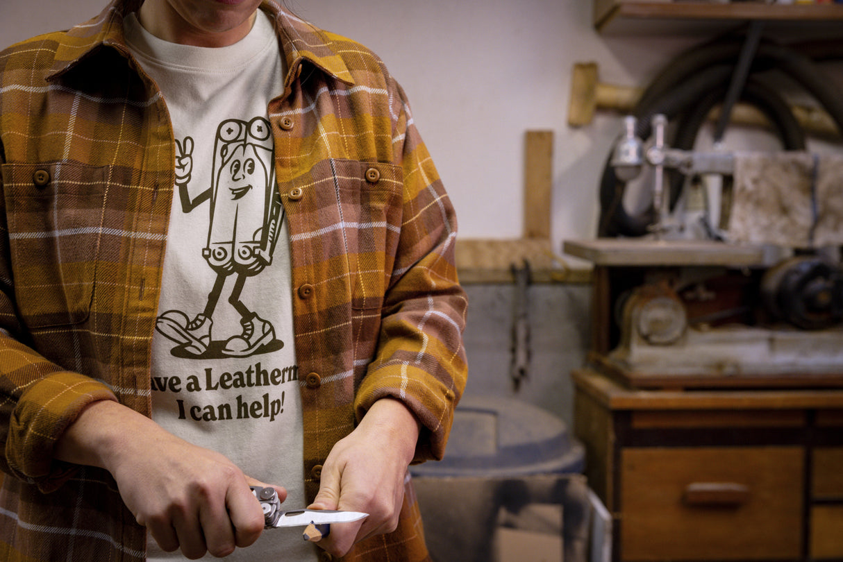 Translation missing: es.A person wearing a natural-colored Leatherman Mr. Wave Tee with a cartoon multitool design using a Leatherman multitool to sharpen a pencil