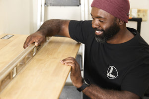 Translation missing: es.A person wearing a black Leatherman Classic Tee using a level tool to level a wooden shelf indoors