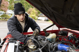 Translation missing: de.A person wearing a black Leatherman Vintage Beanie working under the hood of a red vehicle in a residential driveway