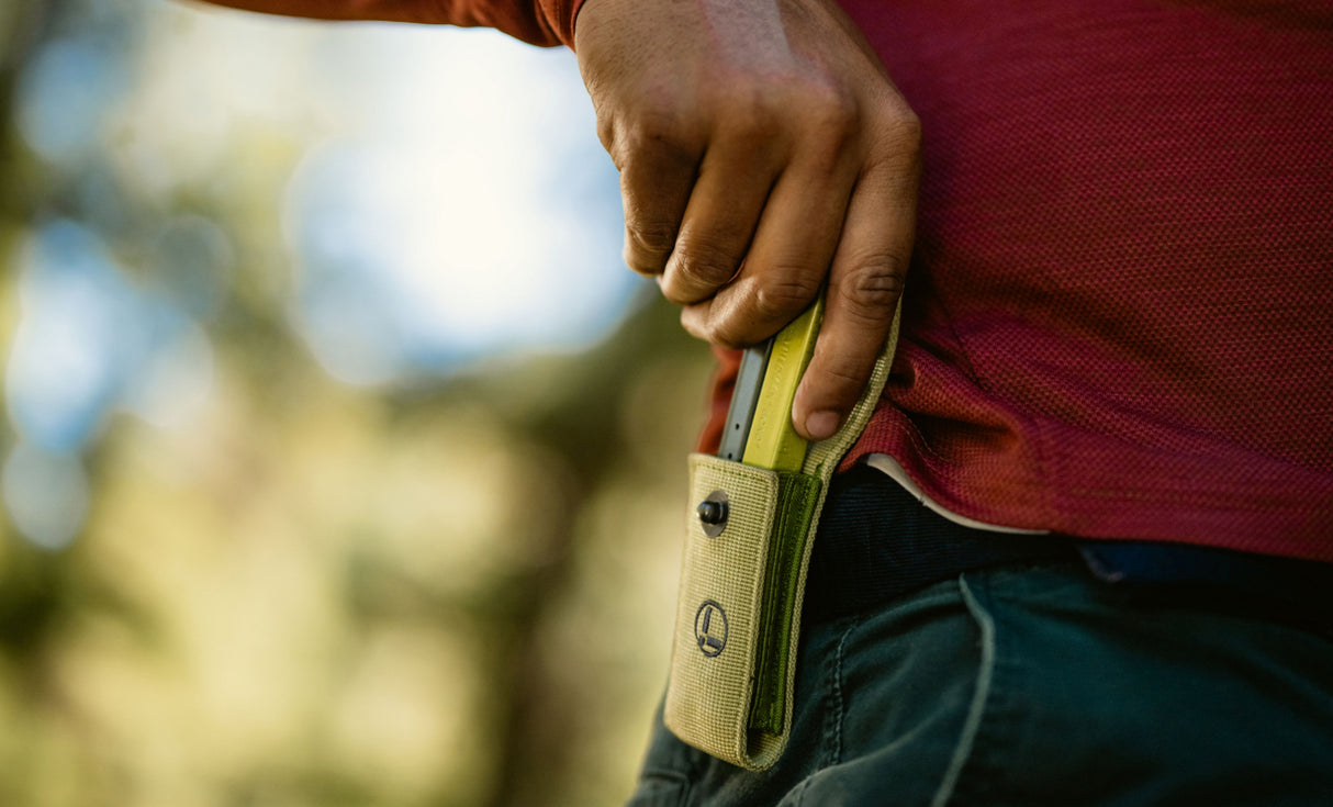Person holding a Mossy Slate Bond half way out of a Moss Sheath that is attached to a belt.