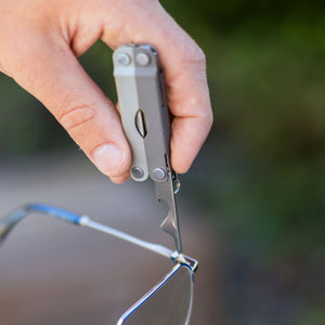Translation missing: es.A Winter Fog colored Leatherman Micra being used to tighten the hinge of a pair of eyeglasses with its flathead screwdriver tool