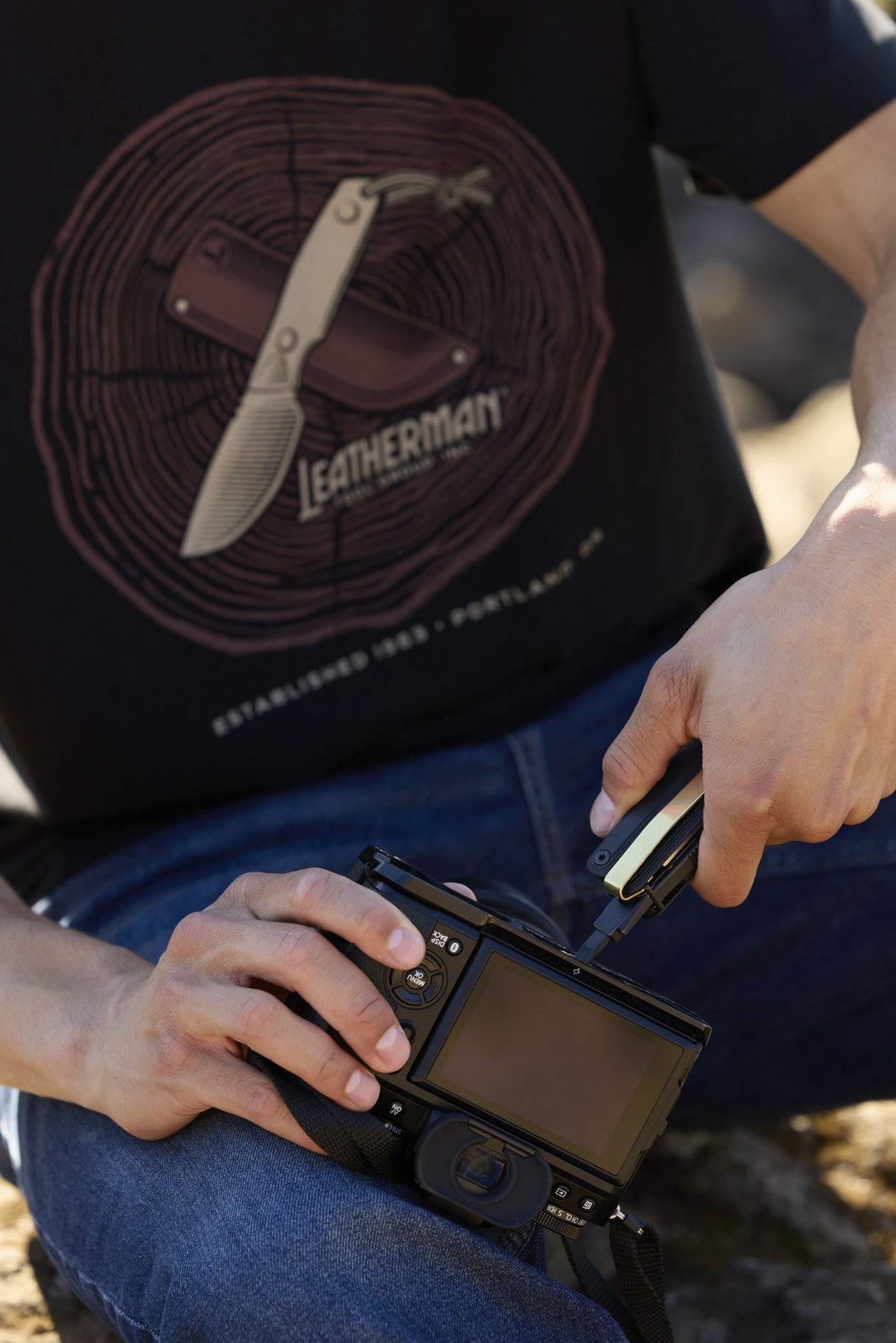 Translation missing: es.A person using a Leatherman Wave Alpha bit driver to tighten a bolt on a camera while wearing a black Blade &amp; Grain Tee