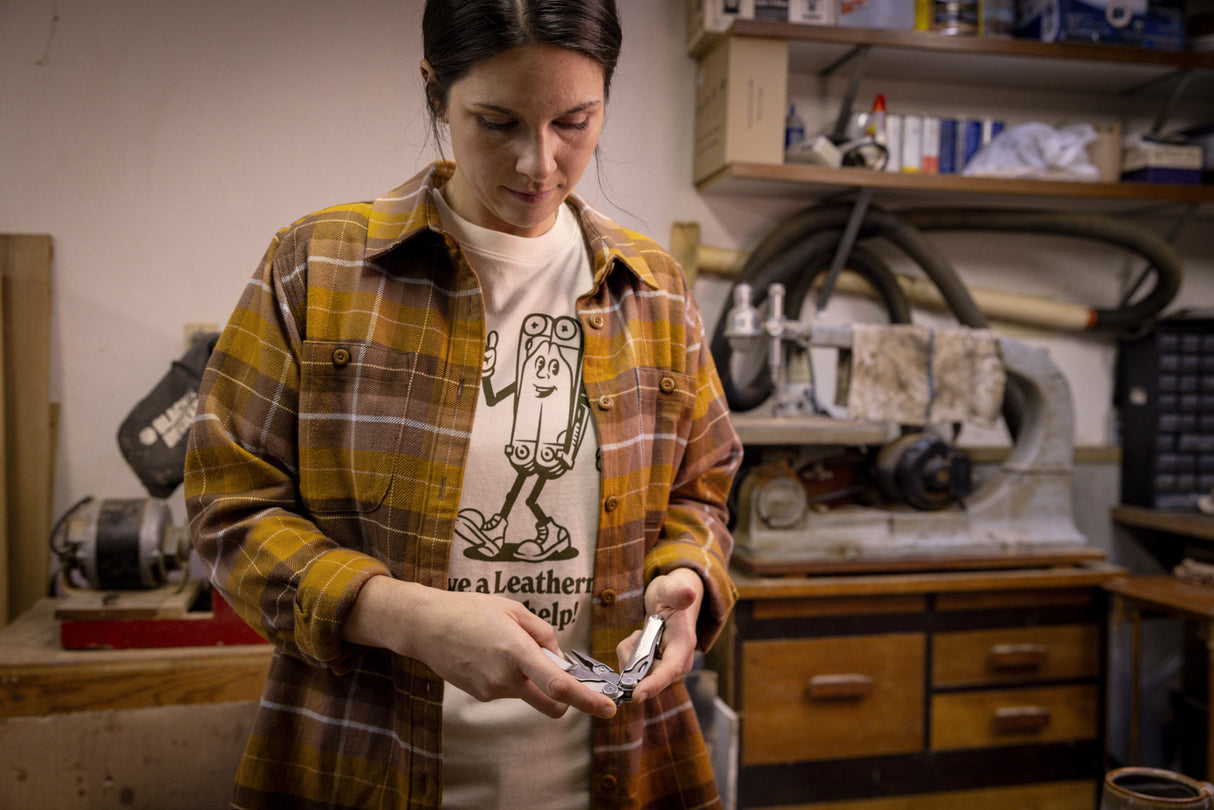 Translation missing: es.A person wearing a natural-colored Leatherman Mr. Wave Tee with a cartoon multitool design opening a Leatherman multitool in a garage