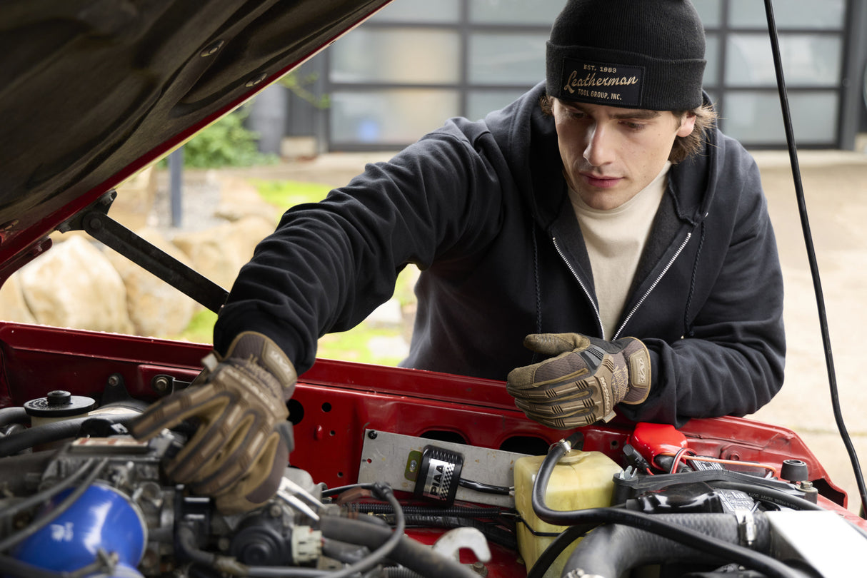 Translation missing: de.A person wearing a black Leatherman Vintage Beanie working under the hood of a red vehicle