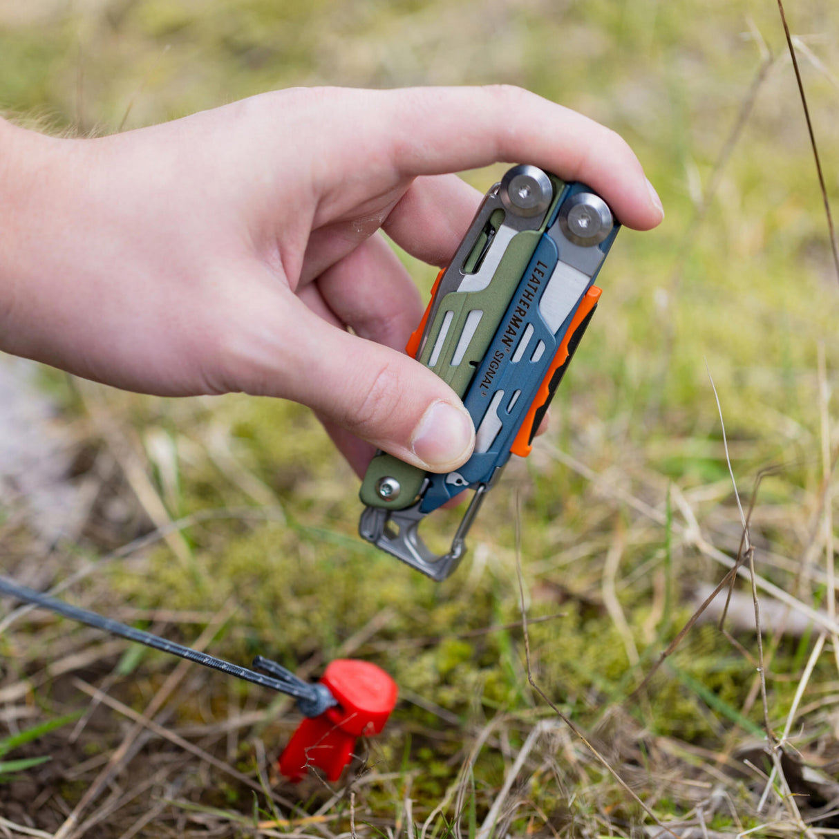 A person uses Leatherman Signal to hammer tent stake in patch of grass.