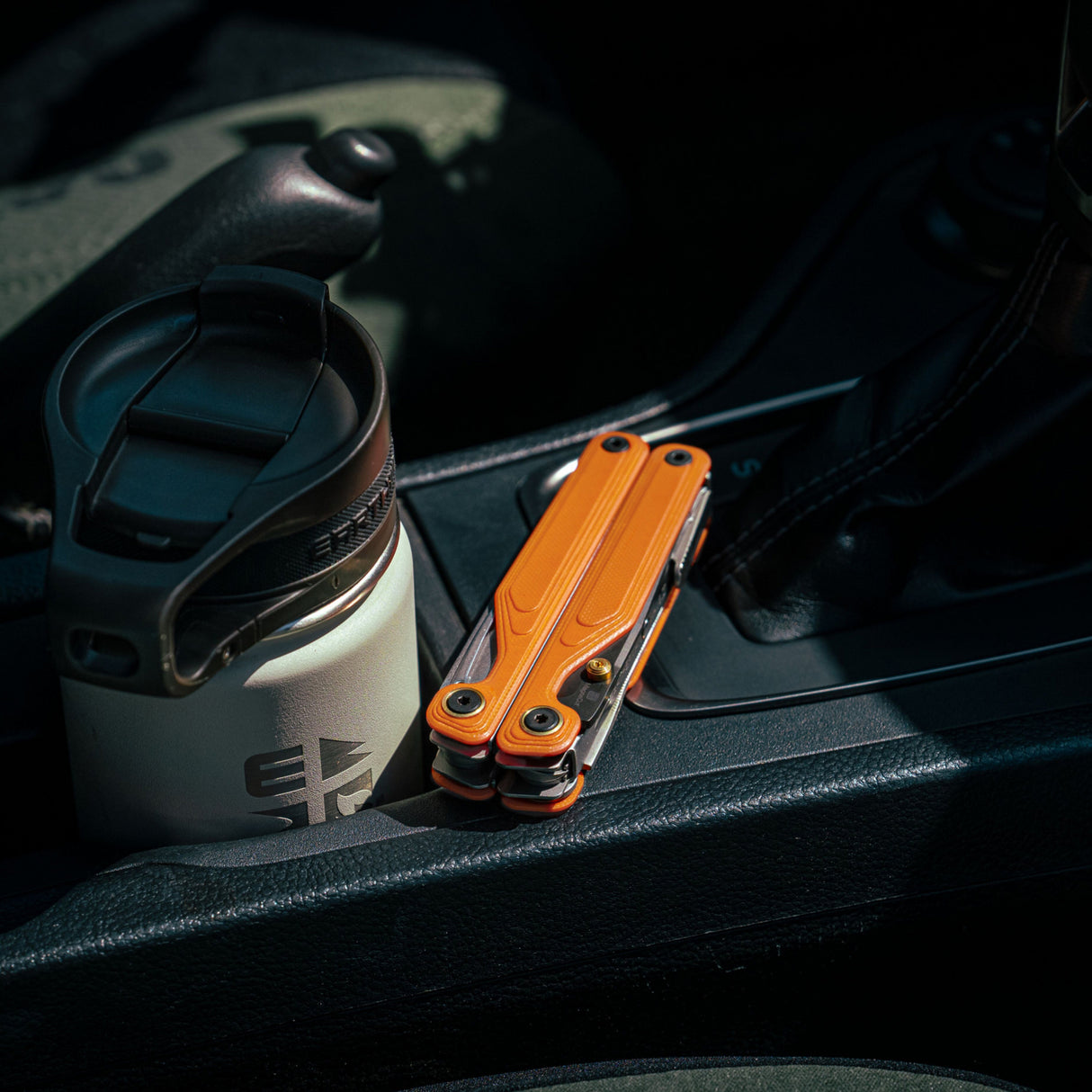 Translation missing: de.Leatherman Wave® Alpha Canyonland multi-tool folded, placed in a vehicle cup holder beside a travel mug