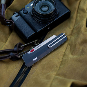 Translation missing: en. A sleek black camera positioned on a surface, next to closed Leatherman Glider
