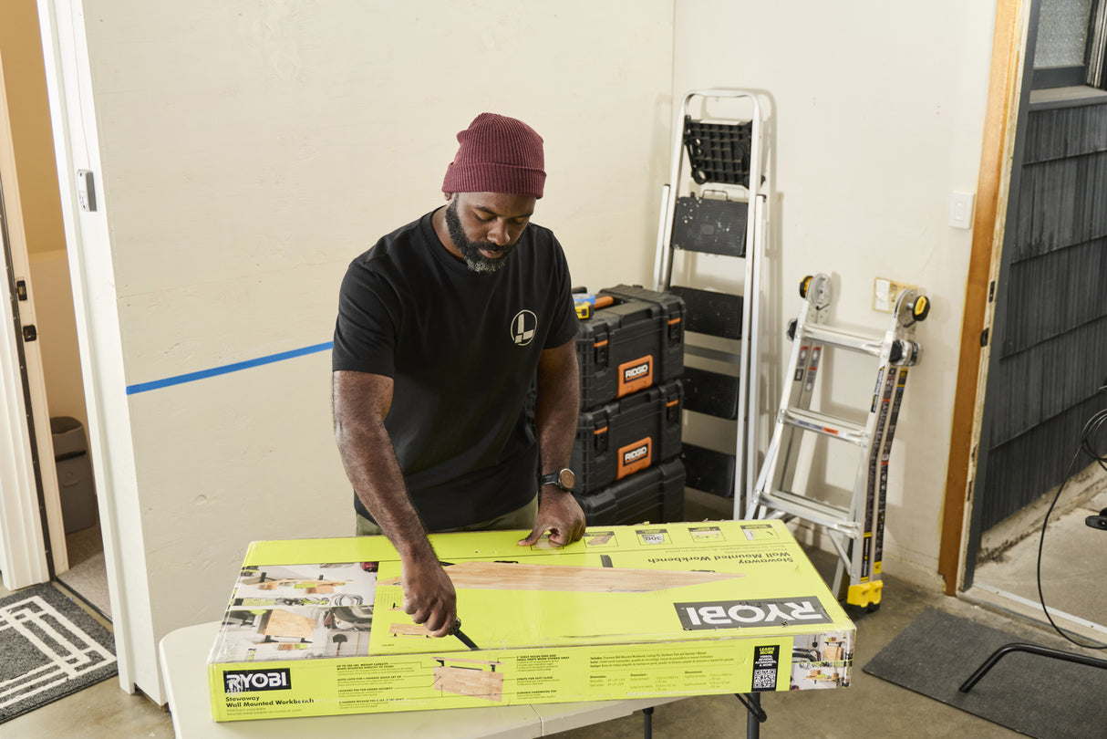 Translation missing: es.A person wearing a black Leatherman Classic Tee using the blade on a Leatherman multi-tool to open a large box that is laying on top of a folding table