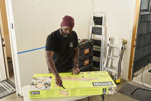 Translation missing: es.A person wearing a black Leatherman Classic Tee using the blade on a Leatherman multi-tool to open a large box that is laying on top of a folding table