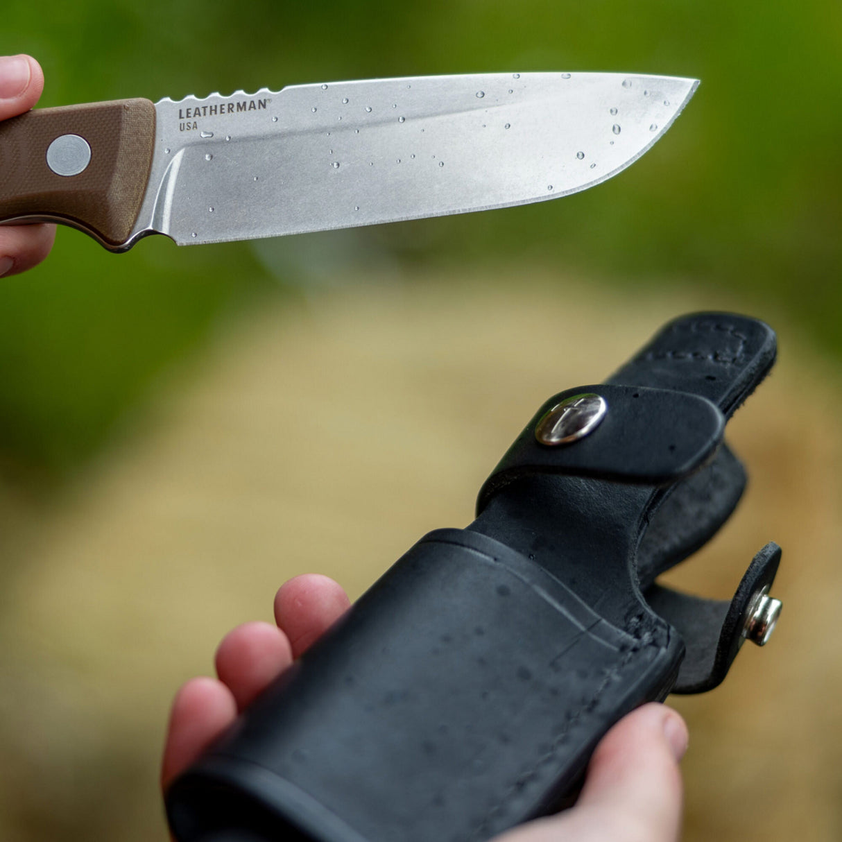 Translation missing: de.Earth Brown Leatherman Trac Knife with water drops on the blade held in one hand, while the Leatherman Trac Knife Sheath with silver snap closures open held in the other hand