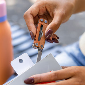 Translation missing: es.Close-up of a hand using a Pumpkin Spice colored Leatherman Micra multi-tool to cut open packaging, showcasing its compact knife and portable size
