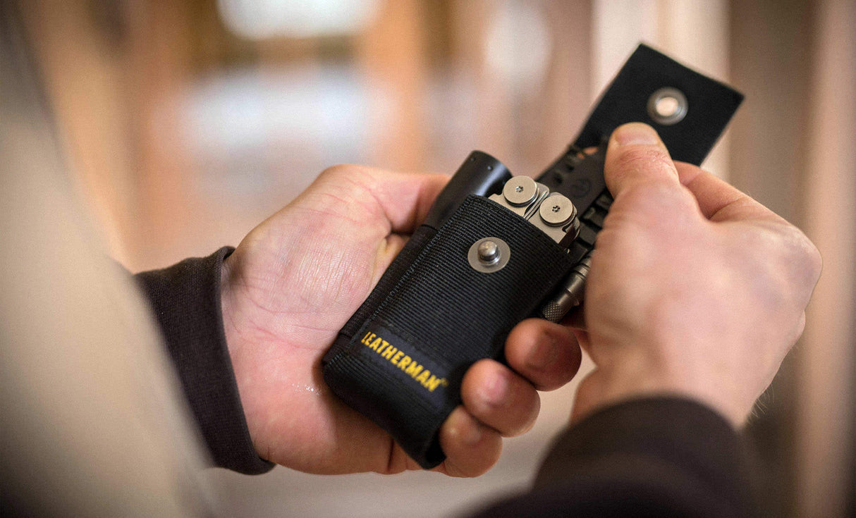 Man pulling Leatherman bit kit from black nylon Leatherman sheath carrying flashlight, Leatherman tool, and Leatherman ratchet driver 