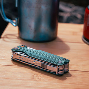 Translation missing: fr.Cascadia Leatherman Wave® Alpha multitool on a wooden surface with camping gear in the background