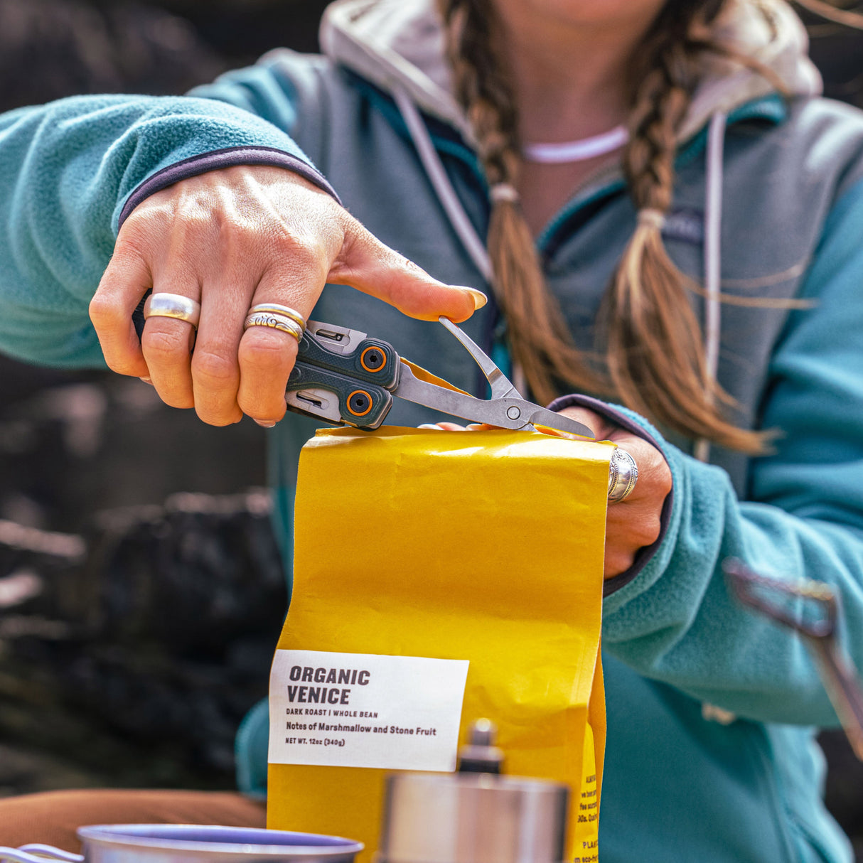Translation missing: fr.Person using the scissors on a Cascadia Leatherman Wave® Alpha to cut open a yellow bag of coffee beans outdoors
