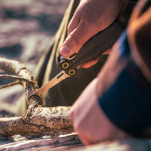 Translation missing: de.Person using the saw on an Obsidian Leatherman Wave® Alpha multitool to cut a branch outdoors