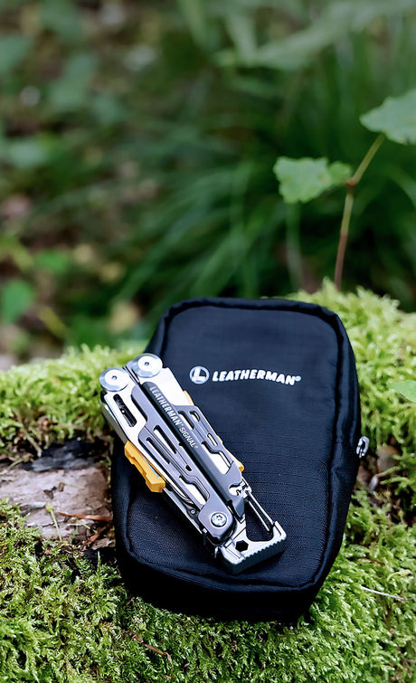 A Leatherman Signal closed laying on a Leatherman Tool Pouch that is on a mossy log.