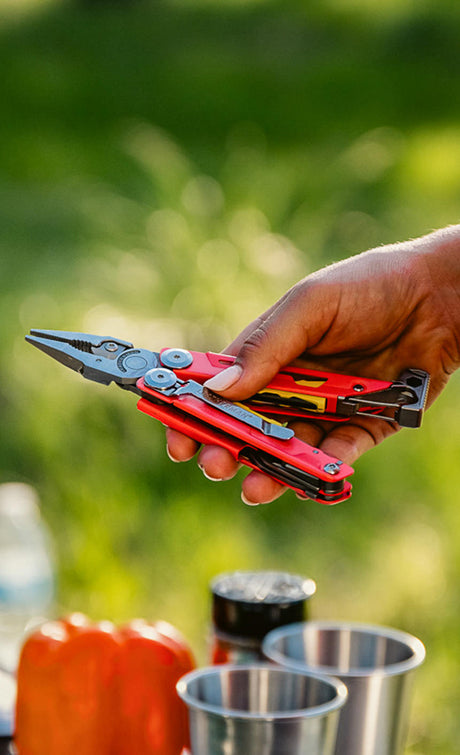 Someone holding a Leatherman Signal in guava color open showing pliers.