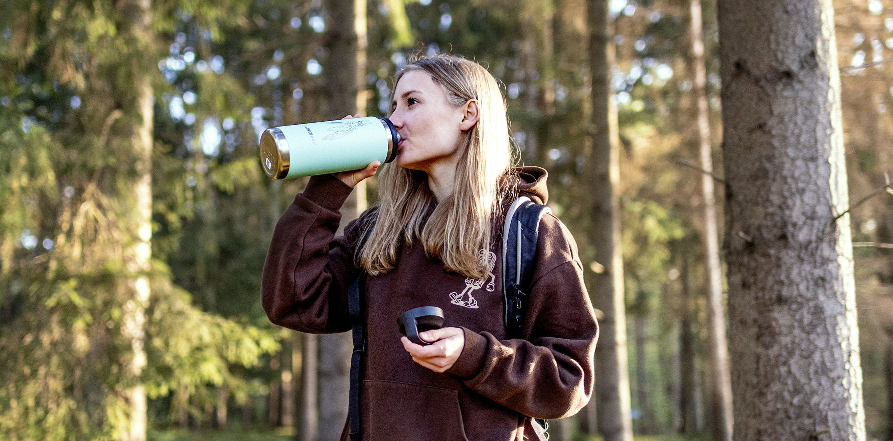 A girl drinking from her Yeti bottle in a lush forest, highlighting outdoor adventure and hydration.