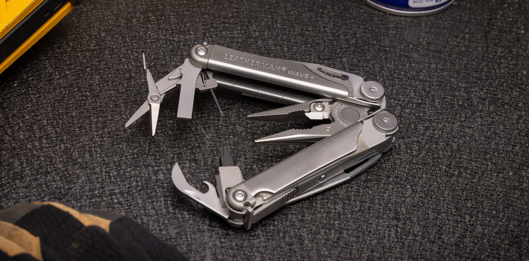 Leatherman Wave Plus multitool with tools fanned on the textured surface of a workbench.