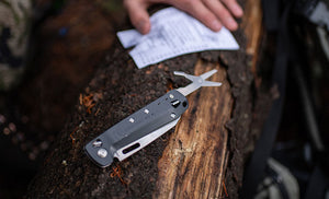 Translation missing: de.Man holding note next to Leatherman K4 with scissors opened on top of tree