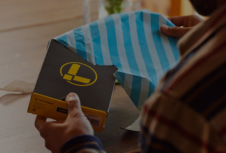 A man unwraps a present containing a Leatherman box.