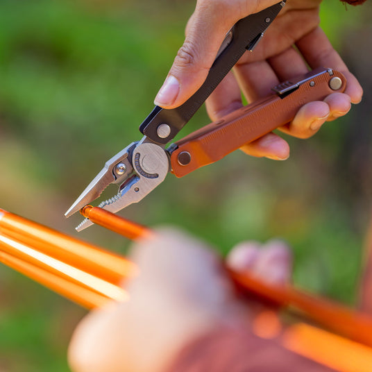 A person cutting a piece of orange wire with Leatherman Bond, focusing on the precise action of the cutting process.