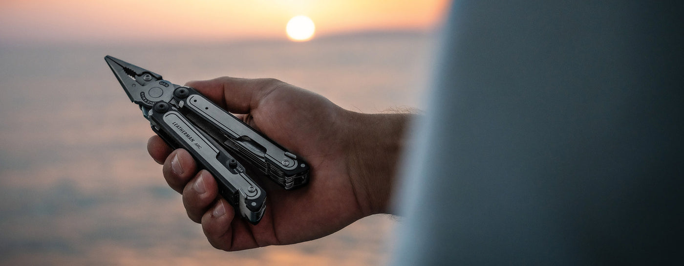 A person stands by the ocean, holding a Leatherman ARC, with waves gently crashing in the background.