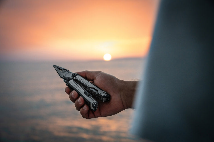 A person stands by the ocean, holding a Leatherman ARC, with waves gently crashing in the background.