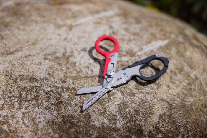A pair of Leatherman shears resting on a textured rock surface, showcasing their sharp blades and sleek design.
