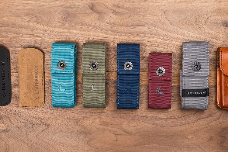 Translation missing: de.A top-down view of ten different Leatherman tool pouches arranged in a row on a wooden surface. The pouches vary in size, material, and color, including black, tan, blue, green, navy, red, gray, brown leather, and black nylon. Some feature snap closures and Leatherman logos, highlighting the variety of carrying options available for multitools