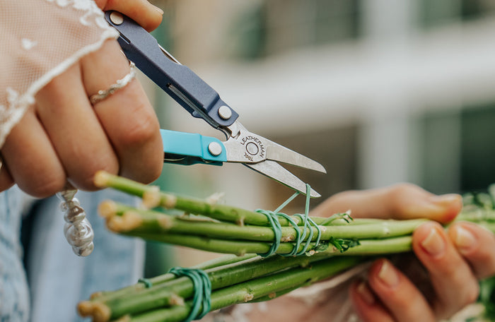 Translation missing: pl.Person using the scissors on a Leatherman Micra® in Lavender Mist color to cut the rubber band holding flower stems