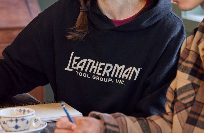 Translation missing: pl.Person wearing a Leatherman Tool Group hoodie while taking notes at a table with a cup of coffee