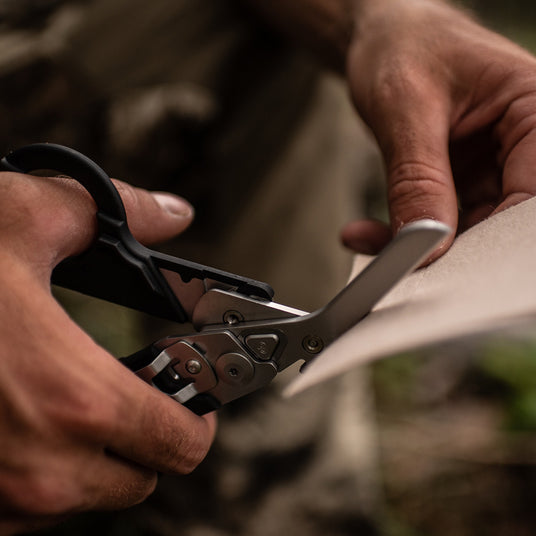 Translation missing: da.Close-up of hands using the scissors on a black Raptor Rescue to cut paper, showcasing focus and precision
