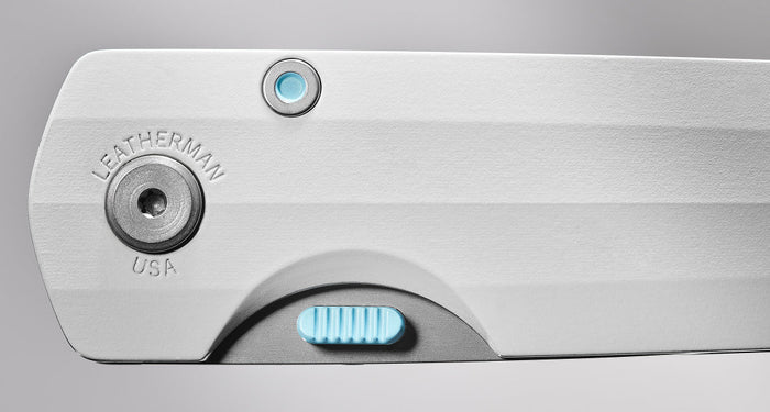 Close-up image of a Leatherman folding knife handle in Alpine white, showcasing precision hardware details, engraved “LEATHERMAN USA” branding, and a textured blue locking mechanism for enhanced control and usability.